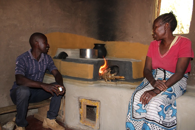Jacob getting the young chicks into the stove warmer while his mother watches as she cooks on the new energy saving jikostove 