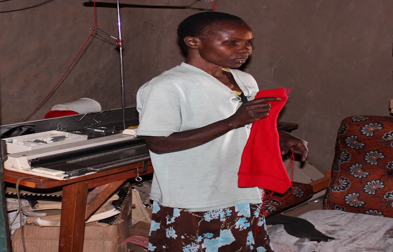 Margaret Kwamboka holding a piece of a legwarmer that she makes using the machine behind her